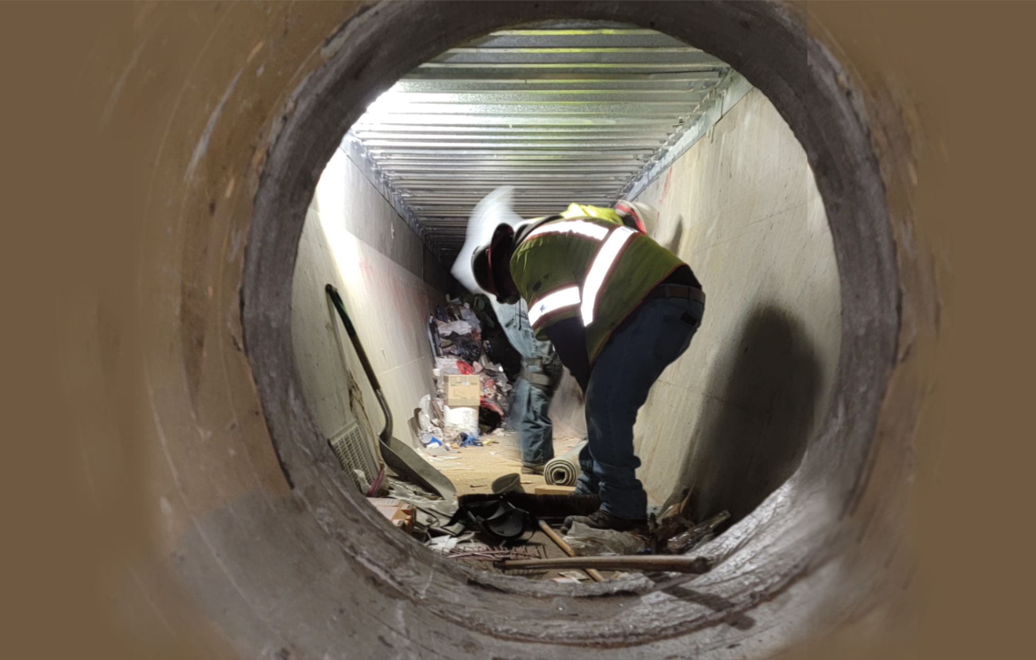 Confined space entry — worker inspecting concrete pipe tunnel